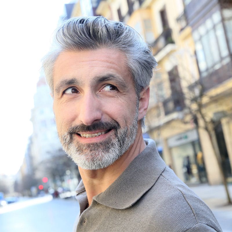 Uomo con barba grigia e sorriso in strada urbana.