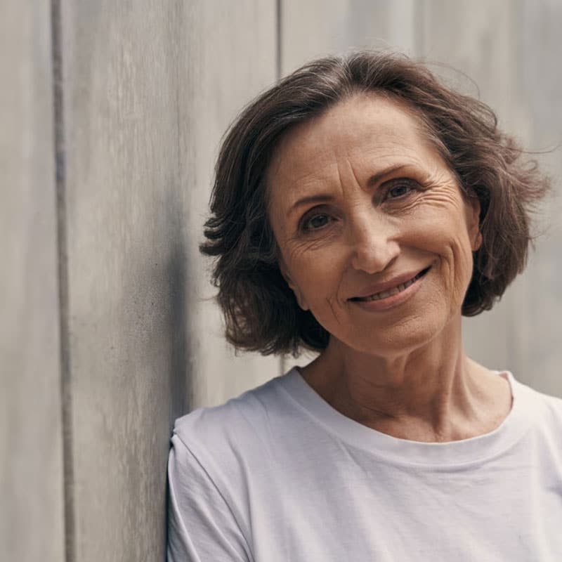 Donna anziana con sorriso sereno, sfondo naturale e ambiente tranquillo.